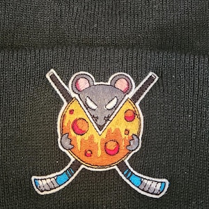 Peut inclure: Bonnet noir avec une image brodée d'une souris portant un maillot de hockey et tenant une part de pizza. La souris porte un maillot noir avec un numéro 1 blanc sur le devant. La part de pizza est jaune avec des pepperoni rouges.