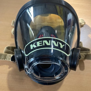 May include: Black firefighter mask with a clear visor and a green label that reads "KENNY".