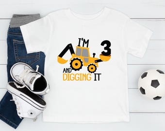 May include: White t-shirt with a yellow and black digger graphic and the text "I'm 3 and digging it".