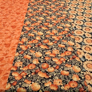 Puede incluir: Un camino de mesa con tres patrones diferentes de temática otoñal. El lado izquierdo presenta hojas naranjas, el medio tiene calabazas y enredaderas, y el lado derecho tiene girasoles.