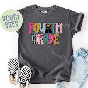 K&ouml;nnte beinhalten: Ein anthrazitfarbenes T-Shirt f&uuml;r Jugendliche mit dem Schriftzug "FOURTH GRADE" in farbenfrohen, verspielten Buchstaben. Das Design umfasst Sterne, Smiley-Gesichter und einen Blitz. Karierte Vans-Schuhe und hellblaue Jeans sind ebenfalls zu sehen.