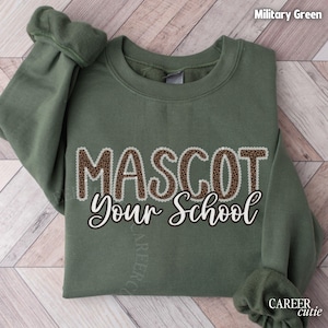 May include: Military green sweatshirt with the text "MASCOT Your School" in a combination of leopard print and white script. The sweatshirt is made of a soft material and has a crew neck.