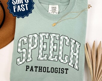 May include: A light green t-shirt with the text "SPEECH PATHOLOGIST" in black letters with a checkered pattern. The text is in a large, bold font and is centered on the shirt. The shirt is made of a soft, comfortable material and is perfect for everyday wear.