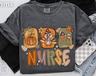 May include: Dark gray long-sleeve shirt with a colorful graphic. The graphic features three rectangular designs with a pumpkin, turkey, and stethoscope. The word "NURSE" is written below in orange, green, and brown letters.