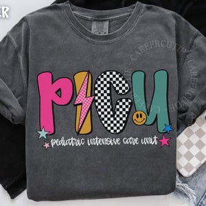 May include: Dark gray sweatshirt with the letters "PICU" in pink, yellow, black and white checkered, and teal. The text "pediatric intensive care unit" is below the letters. A phone with a checkered case is visible.