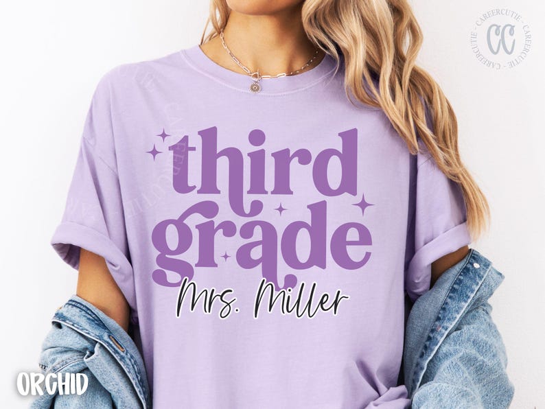 May include: A lilac t-shirt featuring the words "third grade" in a large, purple, retro font, with the name "Mrs. Miller" in cursive. The shirt has a relaxed fit and short sleeves.