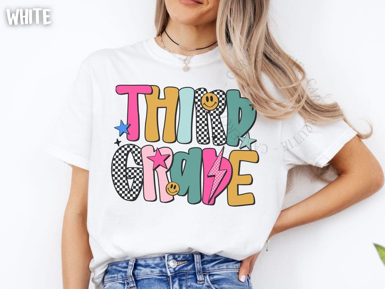 May include: White t-shirt with the words "THIRD GRADE" in colorful, retro-style lettering. The design includes stars, a lightning bolt, and smiley faces. The shirt is a casual, everyday wear item.