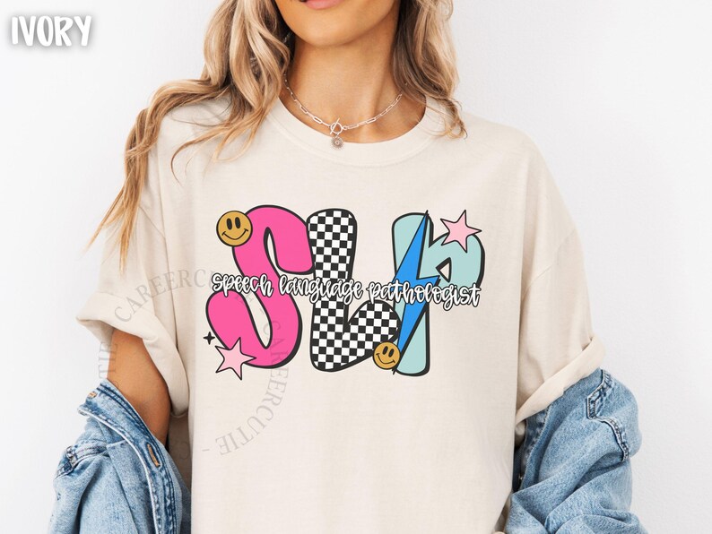 May include: Ivory-colored t-shirt with a colorful graphic design. The design features the letters "SLP" in pink, black and white checkered, and light blue, with the words "speech language pathologist" below. Smiley faces and stars are also included.