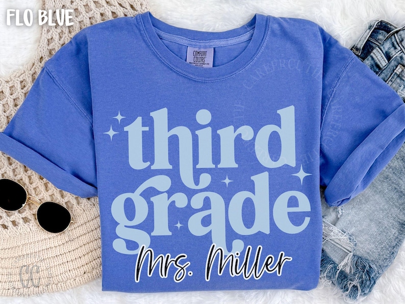 May include: Flo Blue t-shirt with the words "third grade" in light blue, with Mrs. Miller's name below. The shirt has a crew neck and short sleeves. The shirt is made of a soft material.
