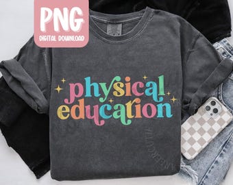 May include: Dark gray long-sleeve shirt with the words "physical education" in colorful, retro-style lettering. The shirt has a crew neck and a relaxed fit. A phone with a checkered case is visible.
