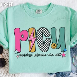 May include: A light green t-shirt with the letters PICU in pink, gold, black and teal. The shirt has a lightning bolt and a smiley face graphic. The text "pediatric intensive care unit" is below the letters.