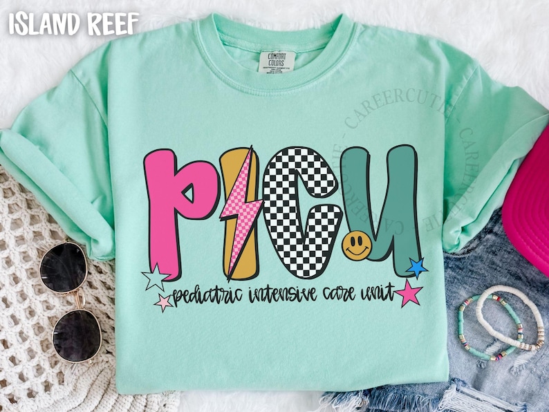 May include: A light green t-shirt with the letters PICU in pink, gold, black and teal. The shirt has a lightning bolt and a smiley face graphic. The text "pediatric intensive care unit" is below the letters.