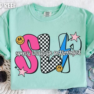 May include: A light green t-shirt with the text "SLP Speech Language Pathologist" in a colorful design. The design includes a pink "S", a checkered "L", and a blue lightning bolt for the "P". Smiley faces and stars are also included.