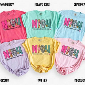 May include: Six colorful t-shirts in shades of pink, blue, yellow, and purple. Each shirt features the word "NICU" in a bold, multi-colored design with a lightning bolt and a smiley face. The shirts are labeled with their respective colors.