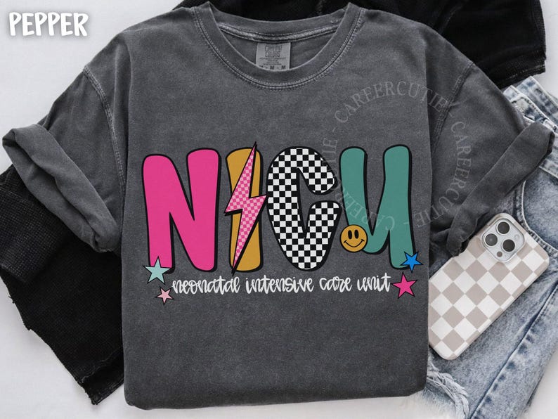 May include: Dark gray sweatshirt with the letters "NICU" in pink, checkered, and teal. A lightning bolt graphic is between the "N" and "C". The text "neonatal intensive care unit" is below the letters. A phone with a checkered case is visible.