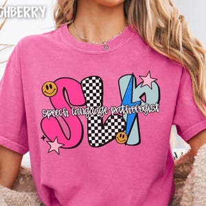 May include: Pink t-shirt with the text "SLP speech language pathologist" in a colorful design. The letters are pink, black and white checkered, and light blue with a lightning bolt. Smiley faces and stars are also included.