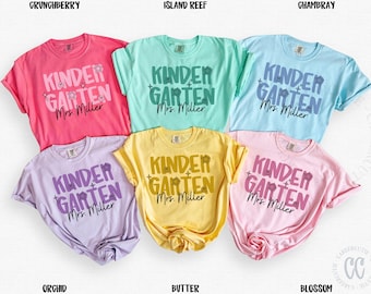 Puede incluir: Seis camisetas de manga corta en varios colores, cada una con la frase "Kindergarten Mrs. Miller" impresa. Los colores incluyen rosa, verde menta, azul claro, lavanda, amarillo y rosa claro. Ropa informal.