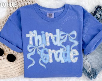 May include: A blue t-shirt with the words "Third Grade" in a playful font, decorated with light blue bows. The text has a patterned design. The shirt is a comfort colors brand.