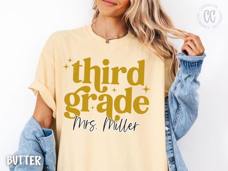 May include: Pale yellow t-shirt featuring the text "third grade Mrs. Miller" in gold. The shirt has a casual style and is paired with a denim jacket. The text is in a retro font.