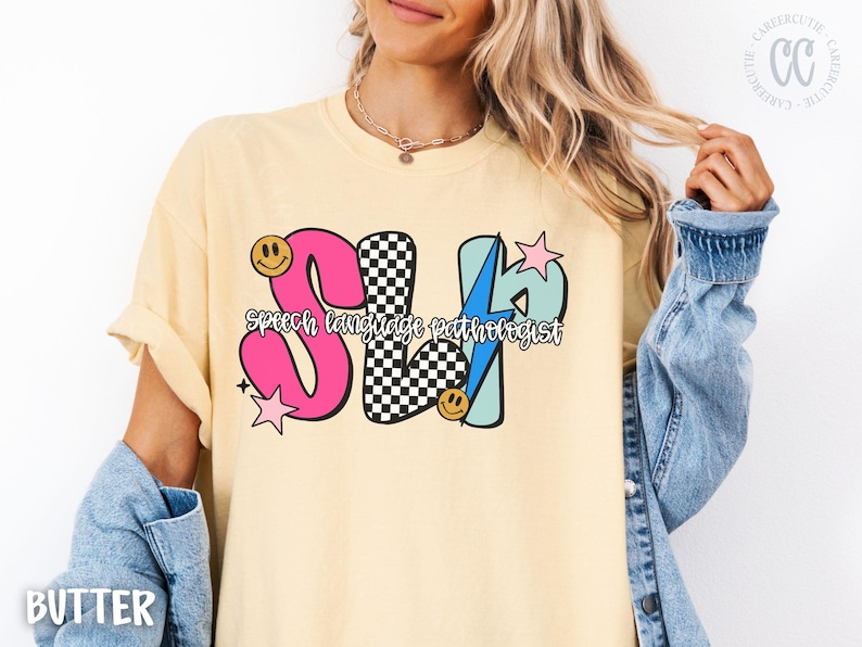 May include: Butter-colored t-shirt with a colorful graphic that says "SLP Speech Language Pathologist". The design includes a pink "S", a checkered "L", and a blue "P" with stars and smiley faces.