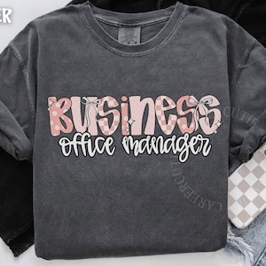 May include: Dark gray comfort colors t-shirt with the words "BUSINESS office manager" in a pink and white design. The word "BUSINESS" has a floral and checkered pattern with bows. The words "office manager" are in a white script font.