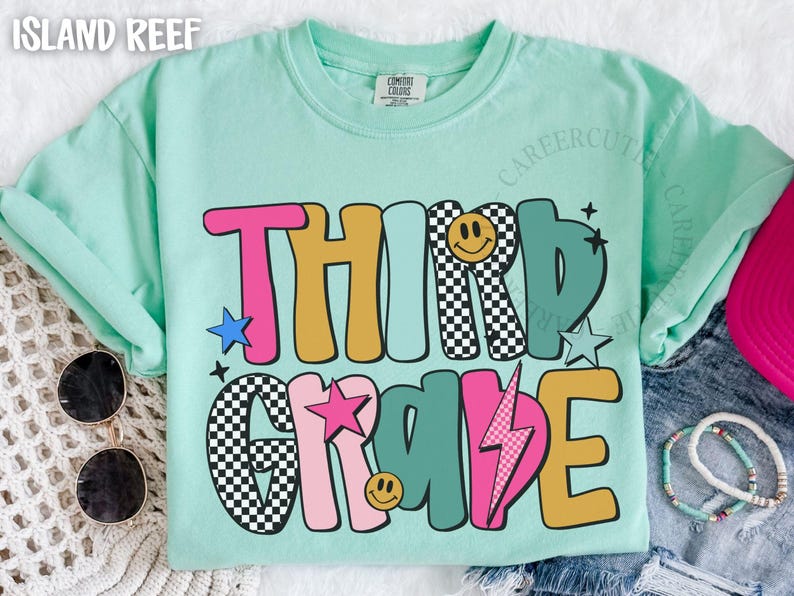 May include: A light green t-shirt with the words "THIRD GRADE" in a colorful, retro font. The design includes stars, a lightning bolt, and smiley faces. Sunglasses and bracelets are visible.