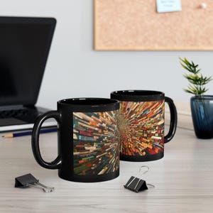 May include: Two black ceramic coffee mugs with a colorful, abstract design. The design features a radial pattern of rectangular shapes in various colors, creating a dynamic and eye-catching visual. The mugs are on a light-colored surface.