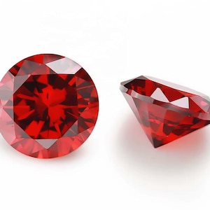 Peut inclure: Deux pierres précieuses rouges, taillées en rond et à facettes. L'une est vue de dessus, l'autre de côté. Les pierres sont d'un rouge profond et riche, avec de nombreuses facettes réfléchissant la lumière.