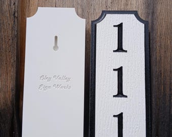 May include: White wooden sign with black trim and the number 111. The sign has a hole for hanging. The back of the sign is blank with the text "Gley Valley Sign Works" embossed in the wood.