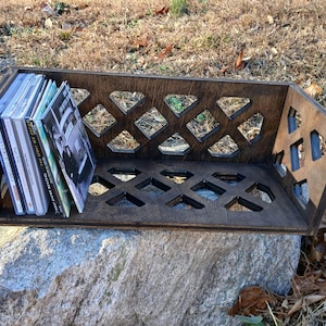 May include: A wooden CD storage shelf with a diamond-shaped lattice design. The shelf is filled with a stack of CDs.