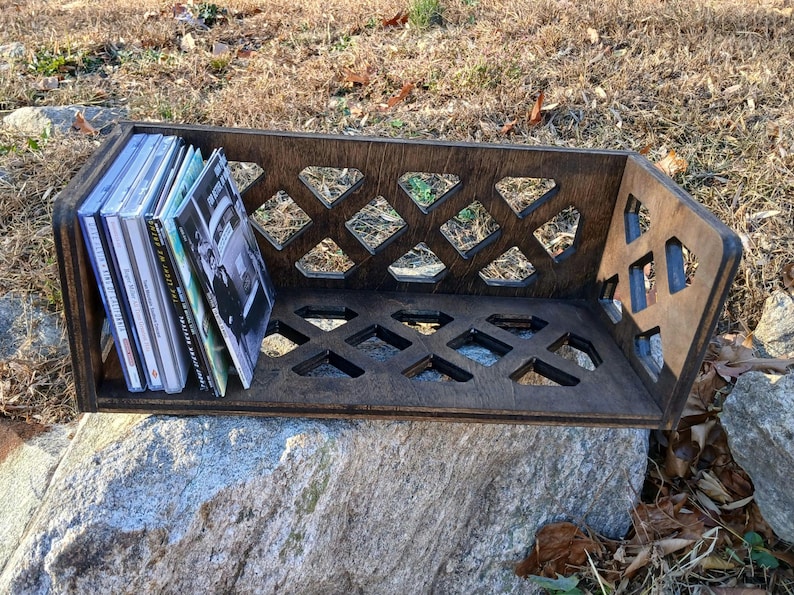 May include: A wooden CD storage shelf with a diamond-shaped lattice design. The shelf is filled with a stack of CDs.