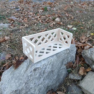May include: A white wooden shelf with a diamond-shaped lattice design. The shelf is sitting on a large grey rock.