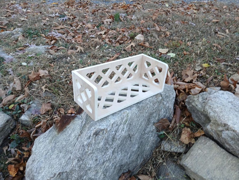 May include: A white wooden shelf with a diamond-shaped lattice design. The shelf is sitting on a large grey rock.