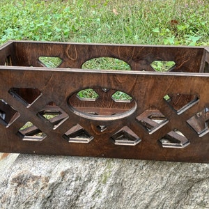 May include: A dark brown wooden storage box with a decorative lattice pattern and an oval cutout. The box is sitting on a rock.