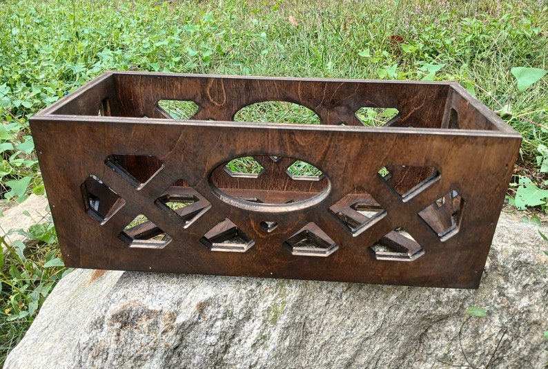 May include: A dark brown wooden storage box with a decorative lattice pattern and an oval cutout. The box is sitting on a rock.