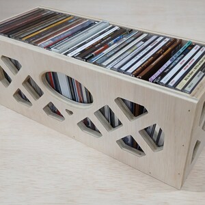 May include: A wooden CD storage box with a geometric pattern cut out of the front and sides. The box is filled with CDs.