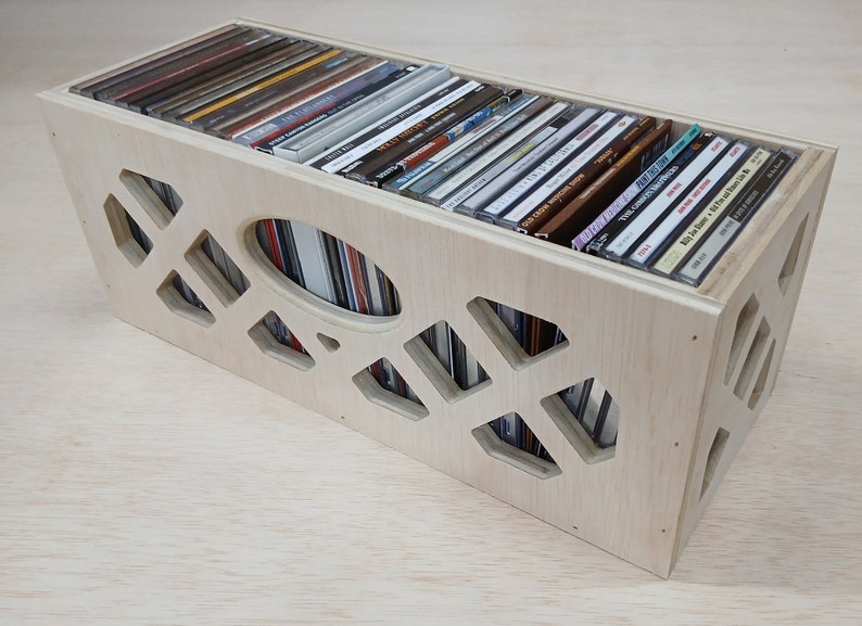 May include: A wooden CD storage box with a geometric pattern cut out of the front and sides. The box is filled with CDs.