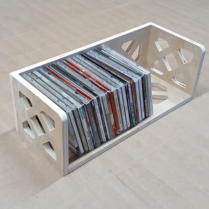 May include: A wooden CD storage rack with a geometric design. The rack is filled with CDs.