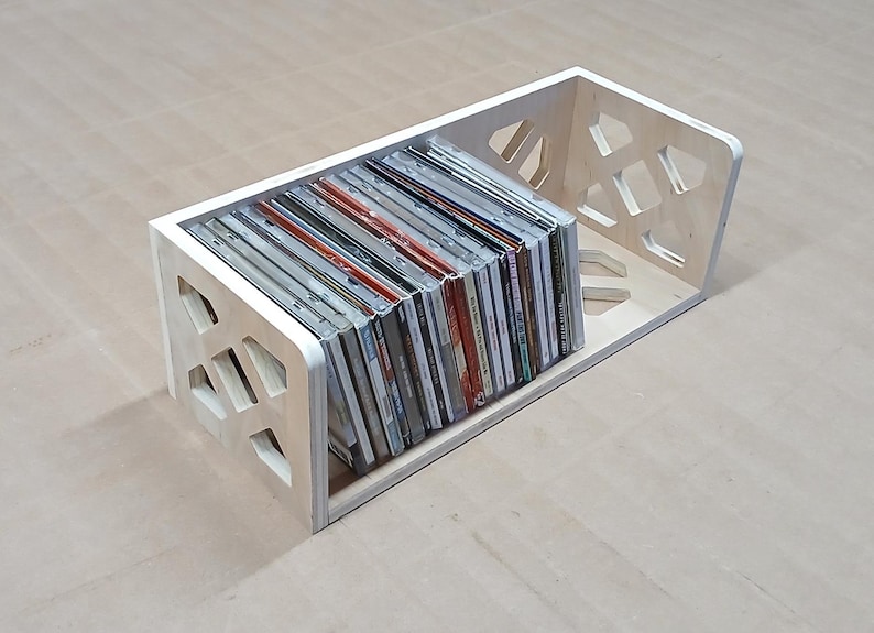 May include: A wooden CD storage rack with a geometric design. The rack is filled with CDs.