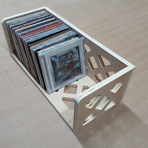 May include: A wooden record storage box with a geometric design. The box is filled with vinyl records.