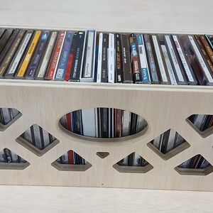 May include: A wooden CD storage box with a cutout design on the front. The box is filled with CDs and has a natural wood finish.