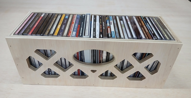May include: A wooden CD storage box with a cutout design on the front. The box is filled with CDs and has a natural wood finish.