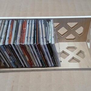 May include: A wooden CD storage rack with a geometric design. The rack is filled with CDs.