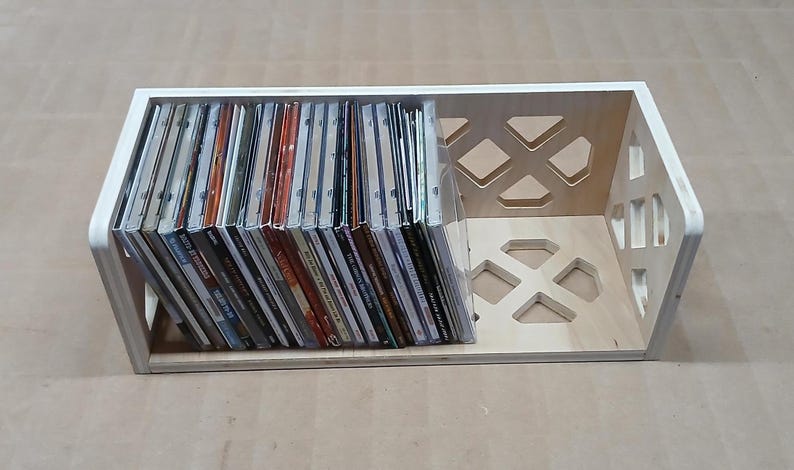 May include: A wooden CD storage rack with a geometric design. The rack is filled with CDs.