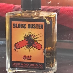 May include: A small, clear glass bottle with a black cap, filled with a golden-brown liquid. The label reads "BLOCK BUSTER" with an illustration of a red object exploding. The bottom of the label says "OIL" and "LUCKY MOJO CURIO CO."