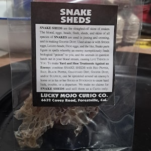 May include: A small plastic bag containing a dried snake shed. The bag has a black and white label with the text "SNAKE SHEDS" and "LUCKY MOJO CURIO CO. 6632 Covey Road, Forestville, Cal."