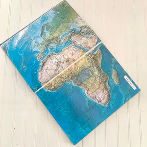 May include: A vintage world map with a blue and green color scheme. The map is folded in half and shows the continents of Europe, Africa, and Asia. The map is titled "Around the Globe".
