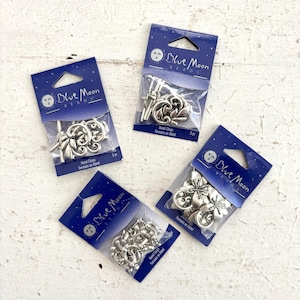 May include: Four packages of Blue Moon Beads metal clasps in various decorative designs. Each package is a dark blue card with the brand name and a clear plastic window showing the clasps. The clasps are silver-colored and feature floral and ornate patterns.