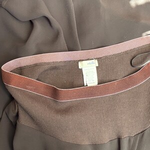 May include: Close-up of a brown garment with a ribbed texture. The garment has a contrasting dark brown band at the top with a thin pink stripe. A tag with the brand name "odille" is visible.