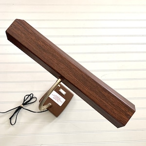 May include: A brown wood-toned desk lamp with a flexible gooseneck arm and a rectangular light fixture. The lamp has a black cord and a white switch.